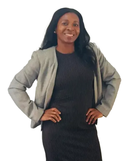 Woman standing with hands on hips, wearing a gray blazer over a black dress, smiling against a white background