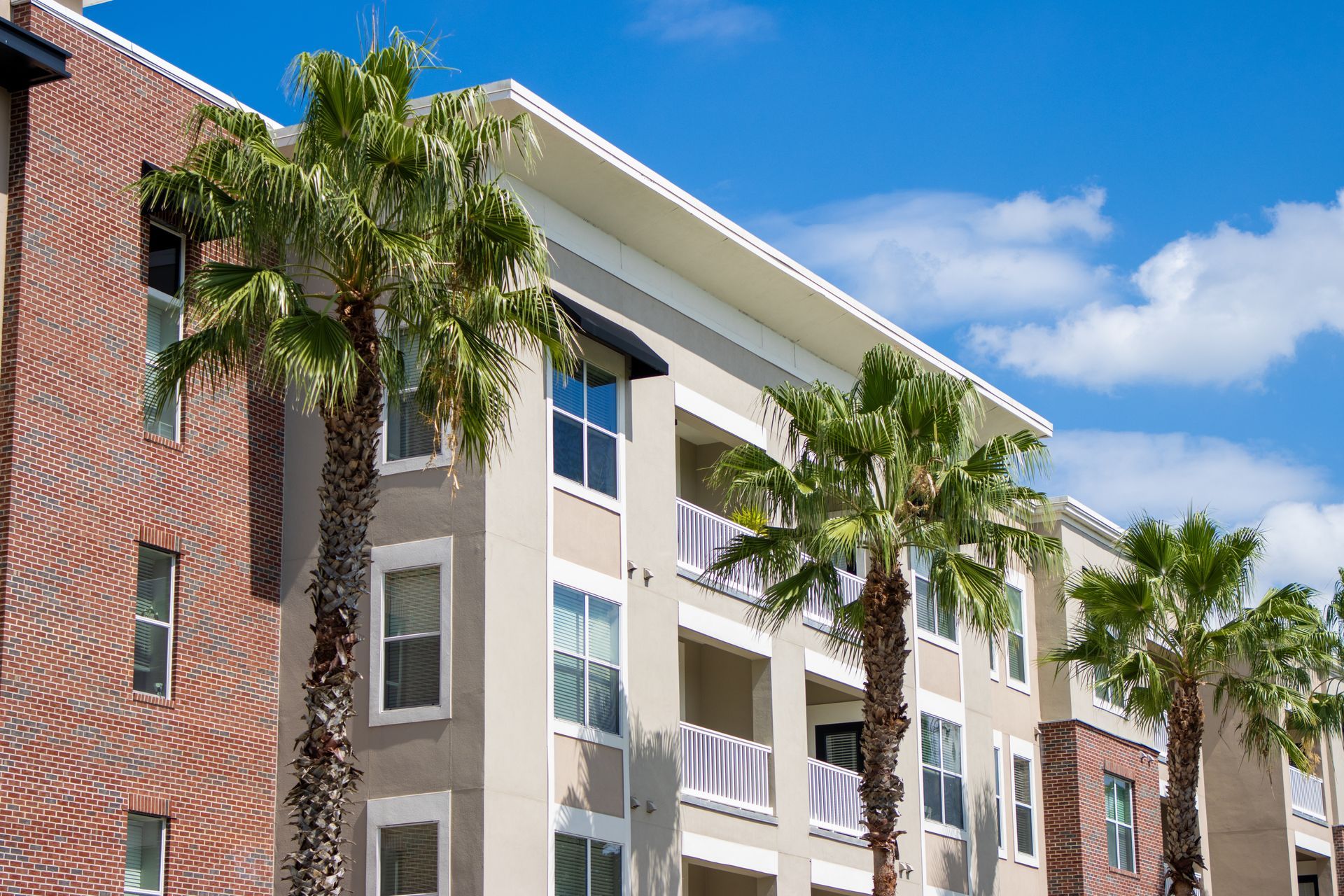 Palm-lined apartment building with red brick and beige siding under a blue sky