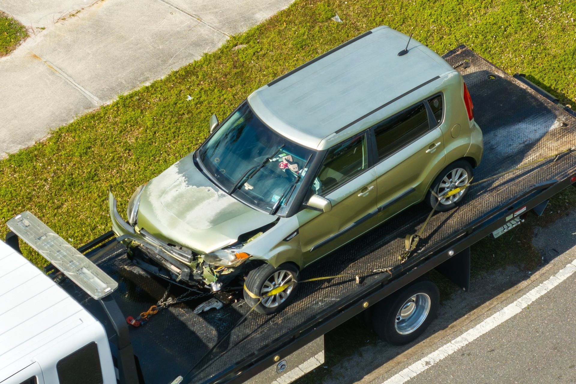 Green hatchback with front-end damage on a tow truck beside a road