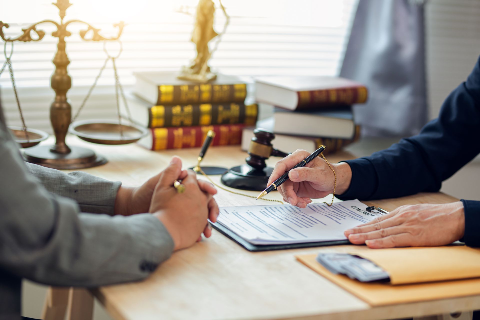 People signing documents at a desk with books and a scale of justice in a law office