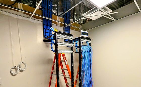 A room with a ladder and a bunch of wires hanging from the ceiling.