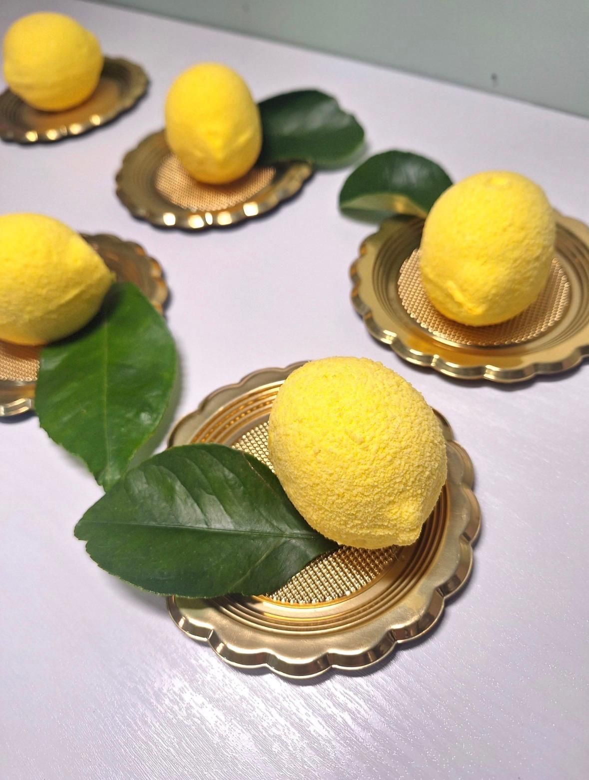 Limoni su sottobicchieri dorati smerlati con foglie verdi, disposti su un tavolo chiaro.