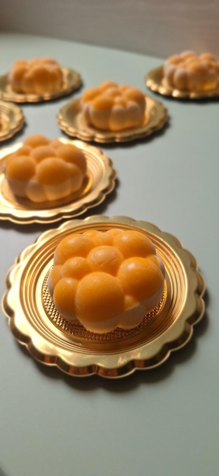 Vassoio di piccoli dessert a forma di cupola arancione su basi dorate smerlate, disposti su una superficie chiara
