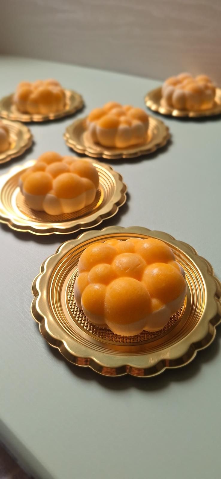 Dessert arancioni a forma di cupola su vassoi dorati smerlati, disposti su un piano di lavoro chiaro.