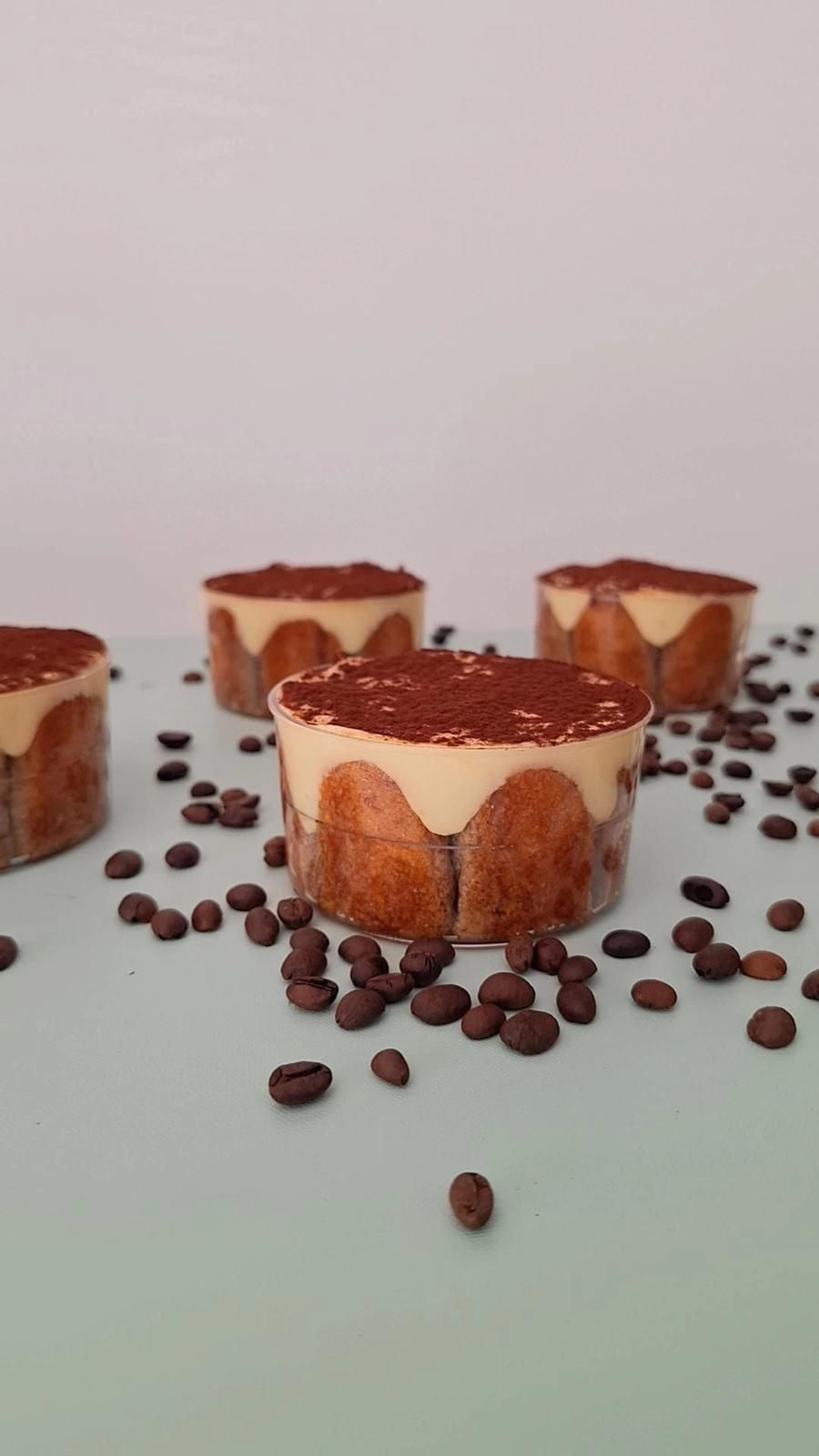 Mini cheesecake al cioccolato con copertura al cacao, disposte su una superficie chiara con chicchi di caffè sparsi.