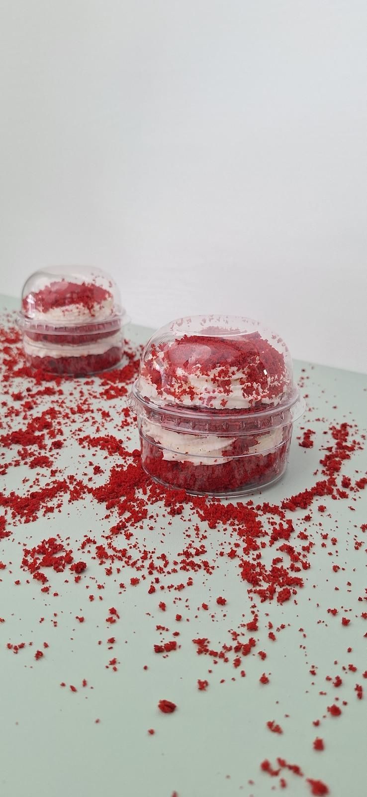 Due vasetti di dessert rossi su una superficie bianca, circondati da briciole rosse sparse