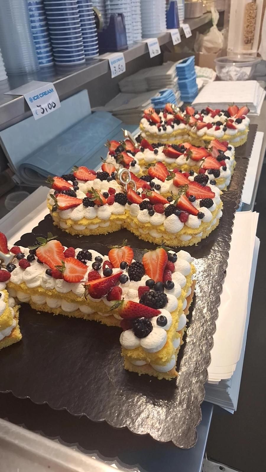 Vassoio di torte decorate con frutta in una vetrina di pasticceria.