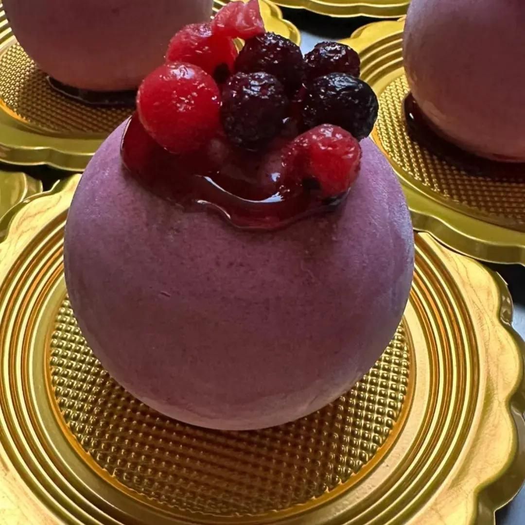 Dessert viola guarnito con frutti di bosco rossi e scuri su un piatto dorato.