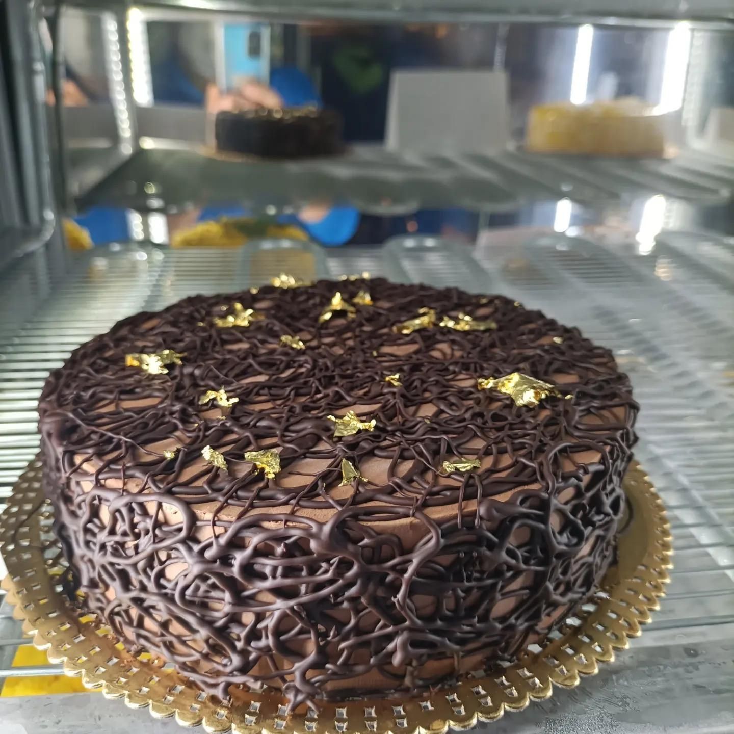 Torta al cioccolato con glassa di cioccolato fondente e decorazioni a forma di stella dorata, su un vassoio dorato in una vetrina.