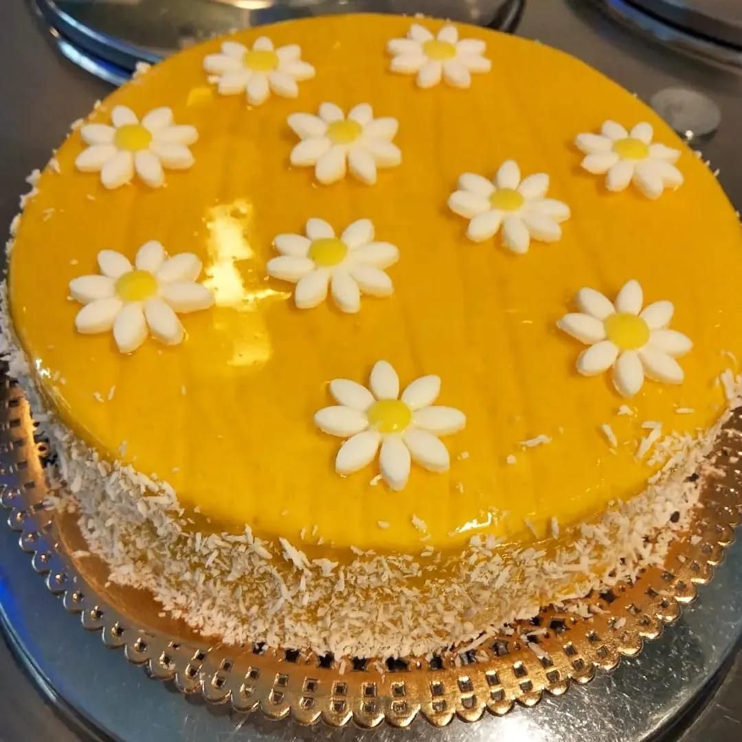 Torta rotonda all'arancia decorata con margherite bianche e cocco grattugiato sui lati.