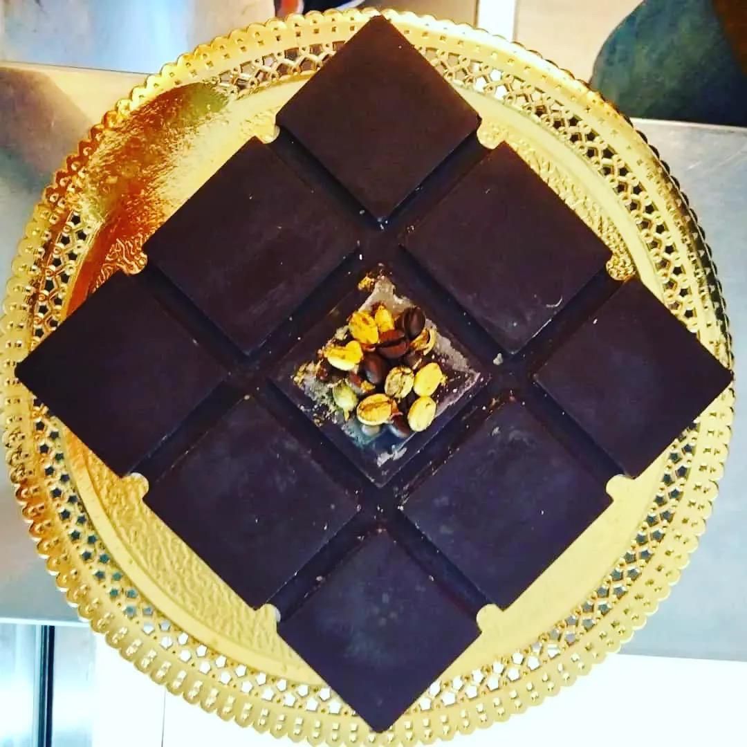 Quadratini di cioccolato fondente disposti a stella su un piatto dorato con noci al centro.