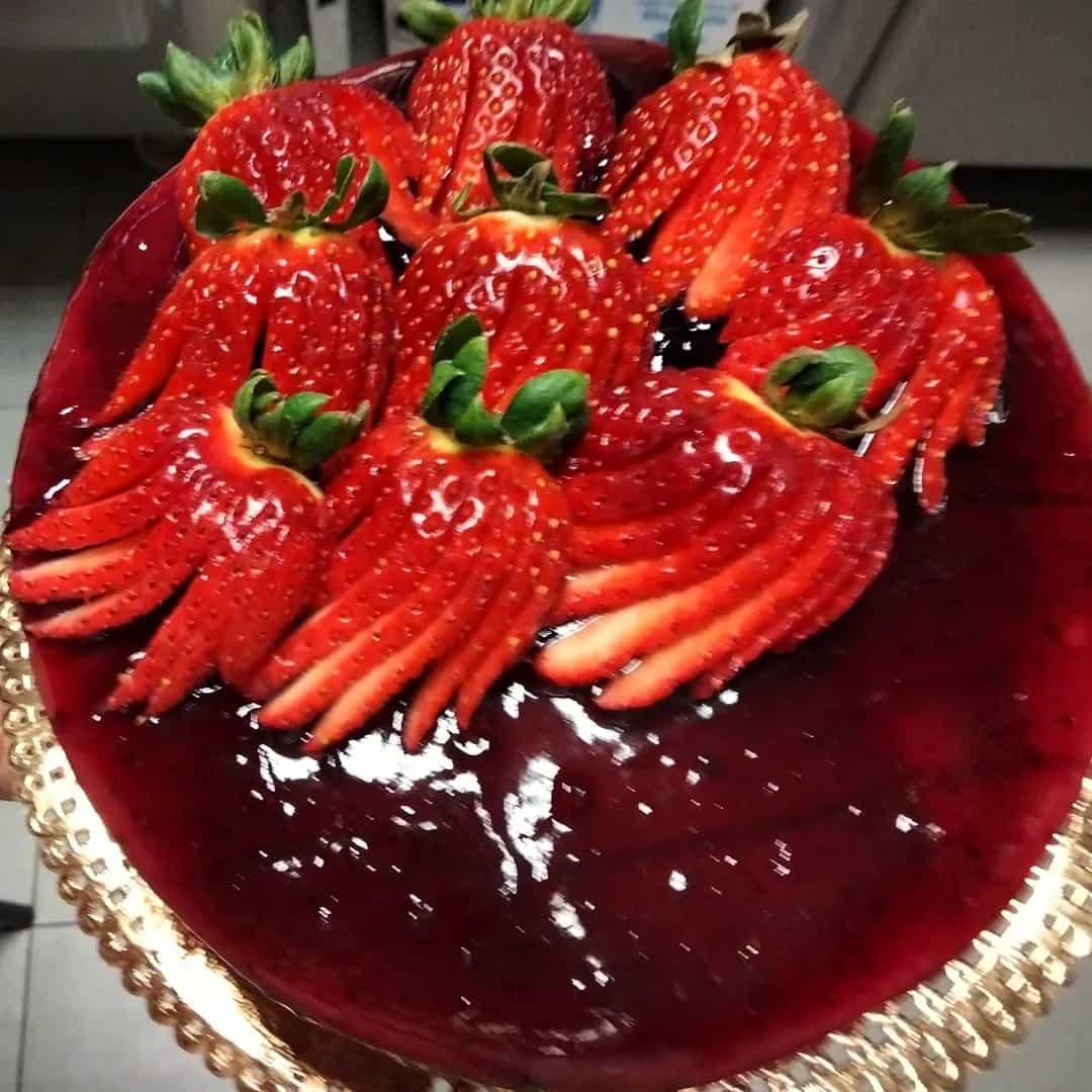 Torta al cioccolato con fragole e glassa scura lucida, servita su un piatto con bordo dorato.