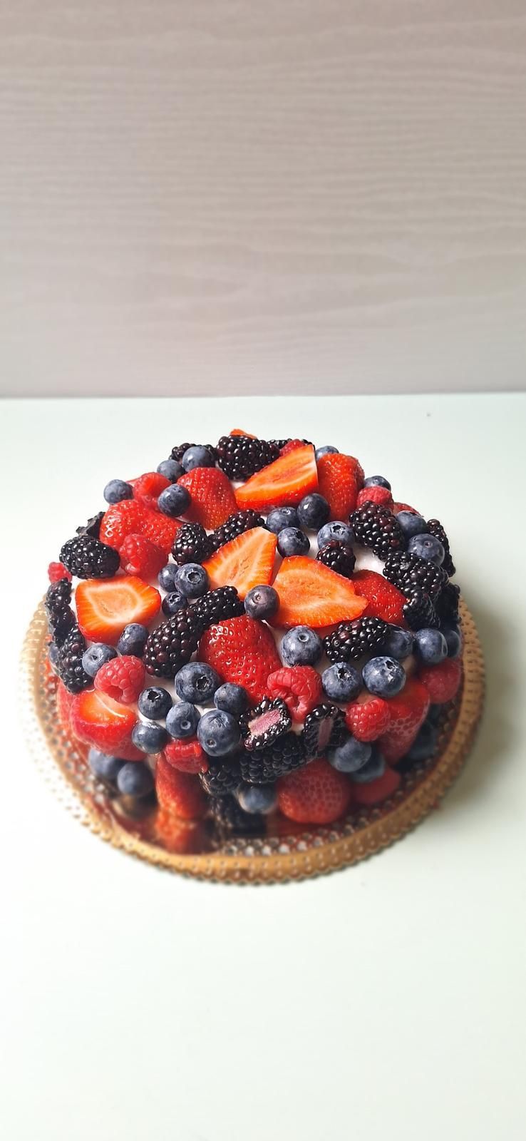 Crostata rotonda di frutti di bosco con fragole, lamponi e mirtilli su una base bianca.