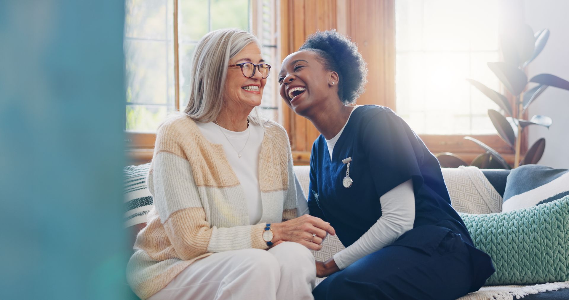 A care worker is sitting beside another adult on a sofa, holding hands during a home care visit