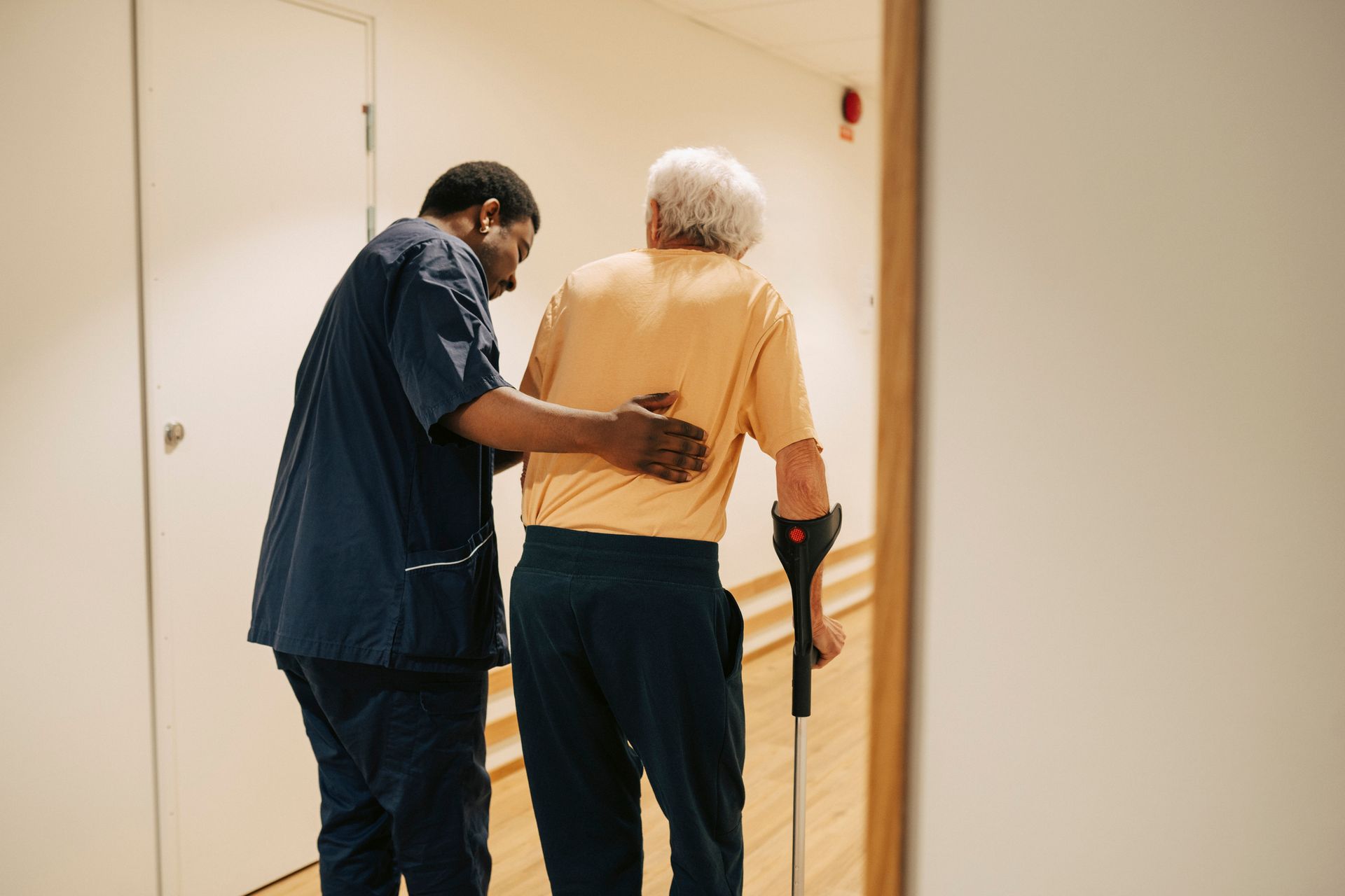 A senior man walking on crutches with the help of a male nurse at a nursing home A senior man walking on crutches with the help of a male nurse at a nursing home