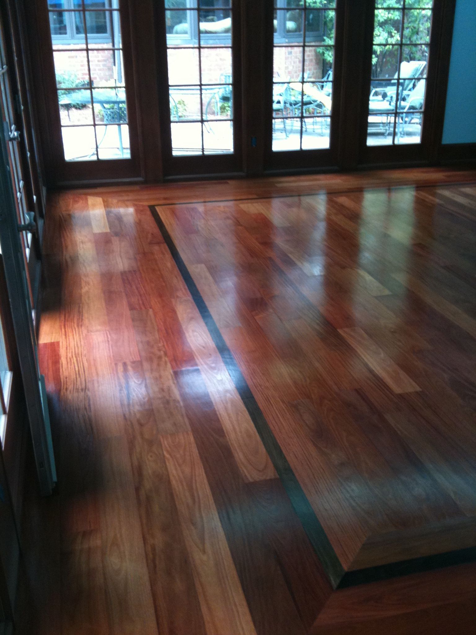 Polished wooden floor in a room with large glass doors and sunlight reflections