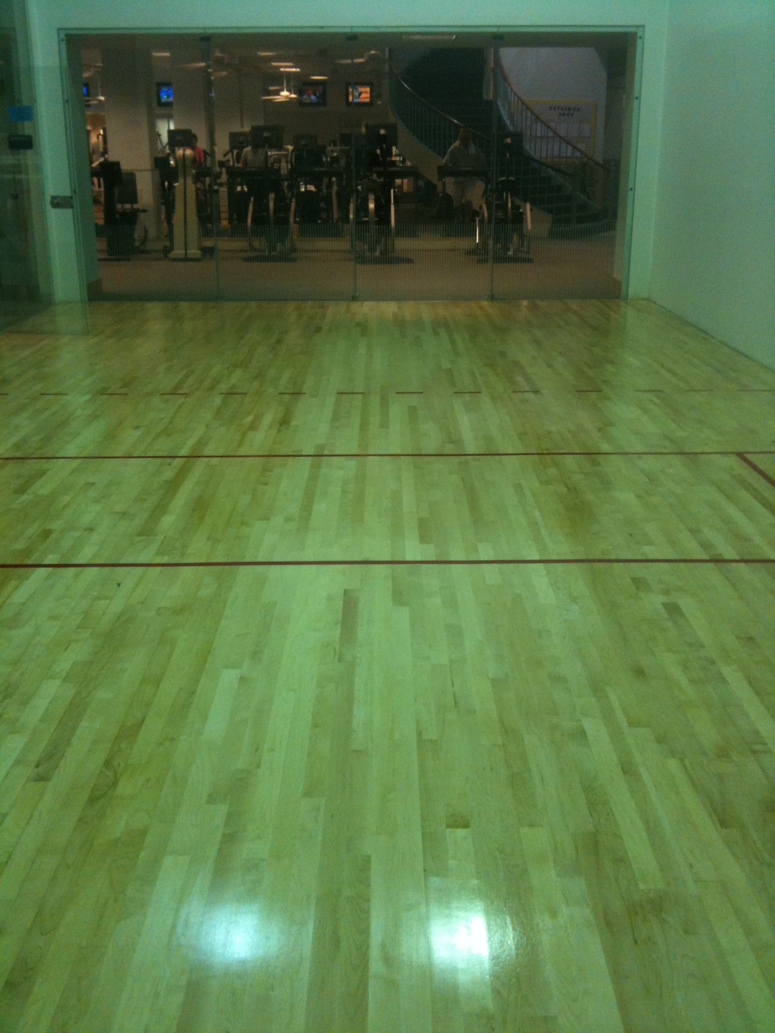 Empty indoor gym with polished wooden floor and glass wall reflection at the far end