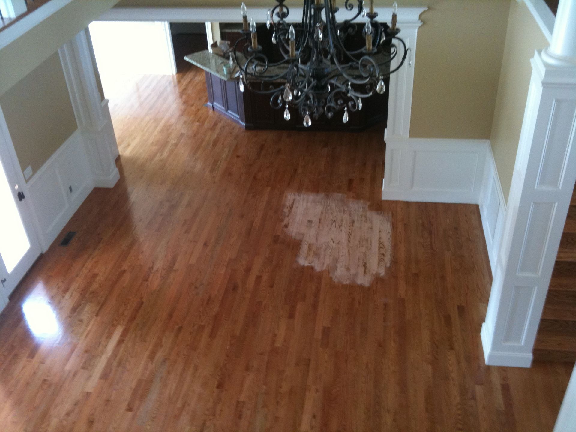 Wooden dining room floor with a discolored patch near a chandelier and doorway