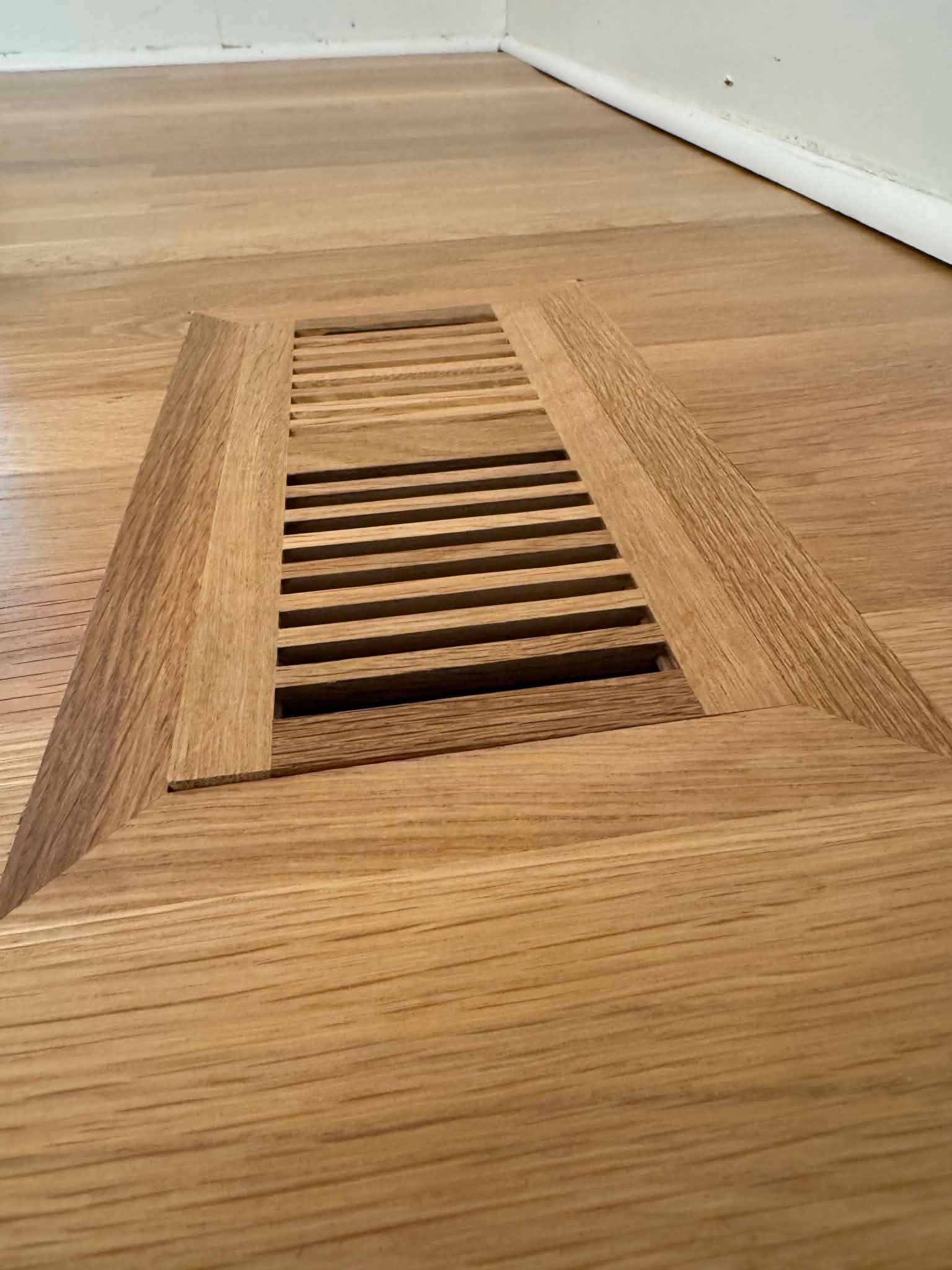 Floor vent grate in a hardwood floor near a white baseboard