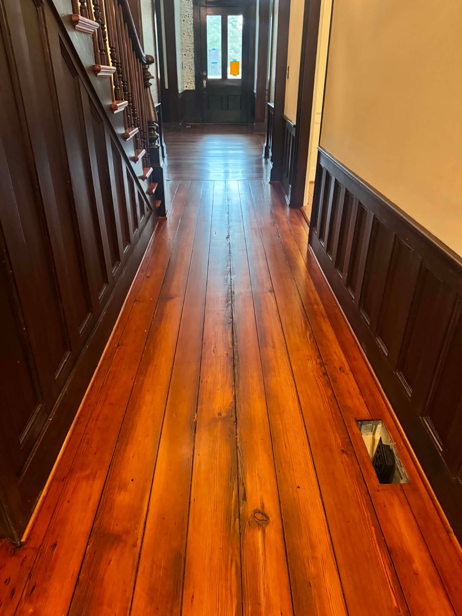 Narrow wooden hallway with polished floor, dark banisters, and a door at the far end.