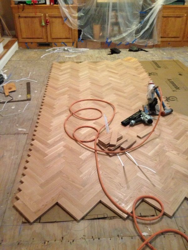 Person painting a dark brown strip along a wall with a yellow paint can on hardwood floor