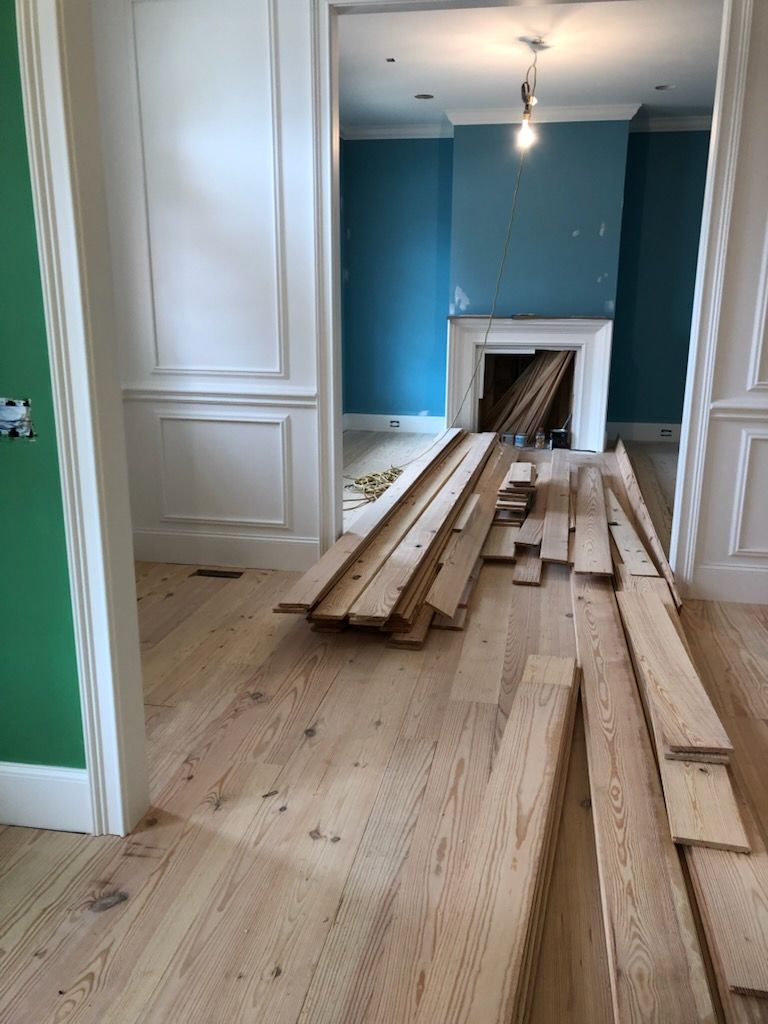 Hallway with stacked lumber on a hardwood floor, leading into a room with blue walls and a fireplace opening