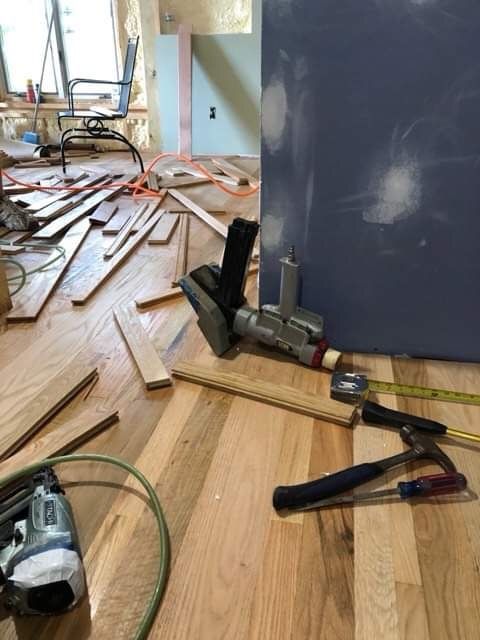 Renovation debris and power tools scattered across a hardwood floor beside a dark cabinet.