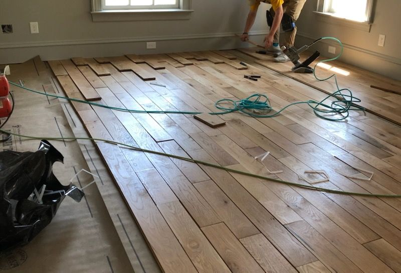 Workers installing hardwood flooring in a sunlit room with tools and wood planks spread across the floor