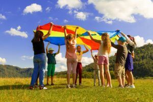 A group of children are holding a colorful parachute in a field.