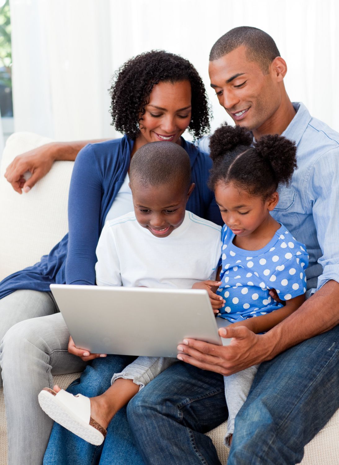 Family of four on a couch looking at a laptop together, smiling.