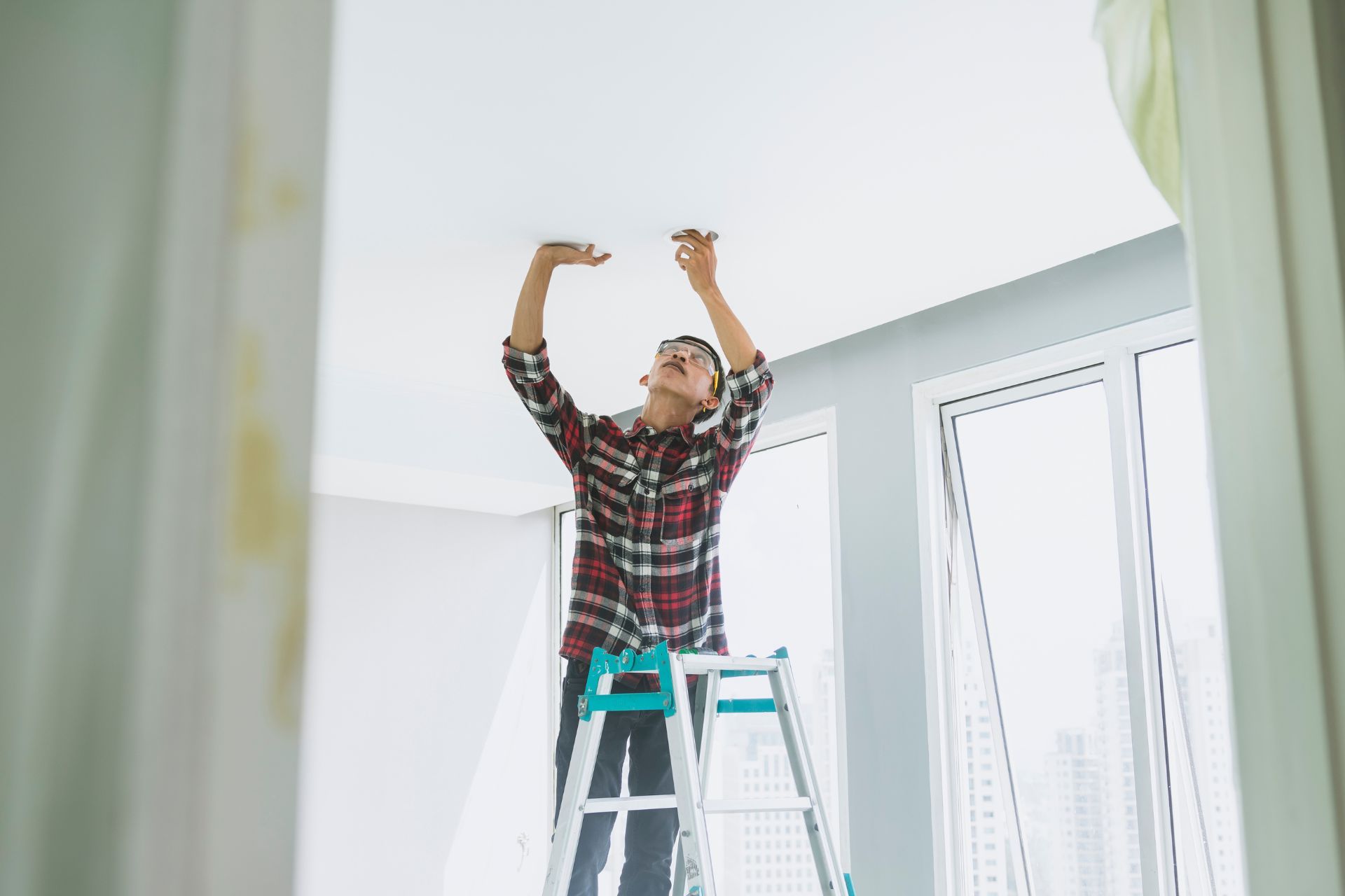 Person on a stepladder installing a light fixture in a room.