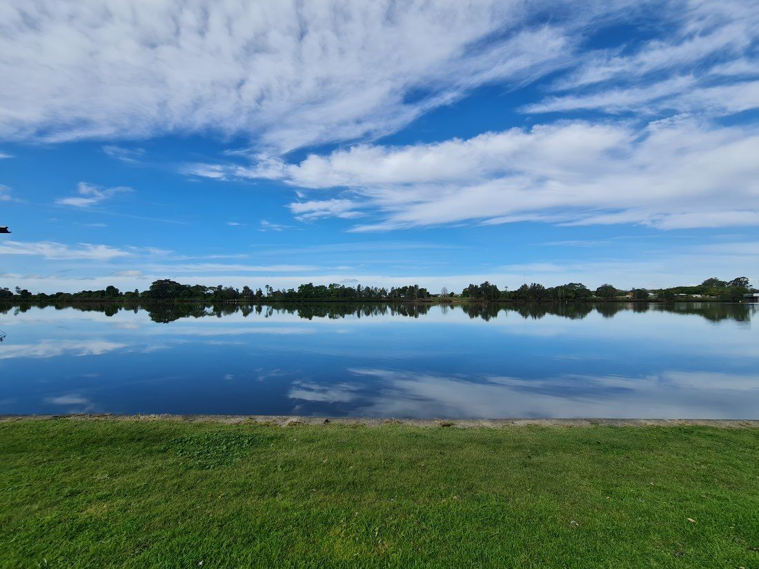 A Large Body Of Water With Trees In The Background And A Blue Sky With Clouds — The Guttering Cleaning Man in Taree, NSW