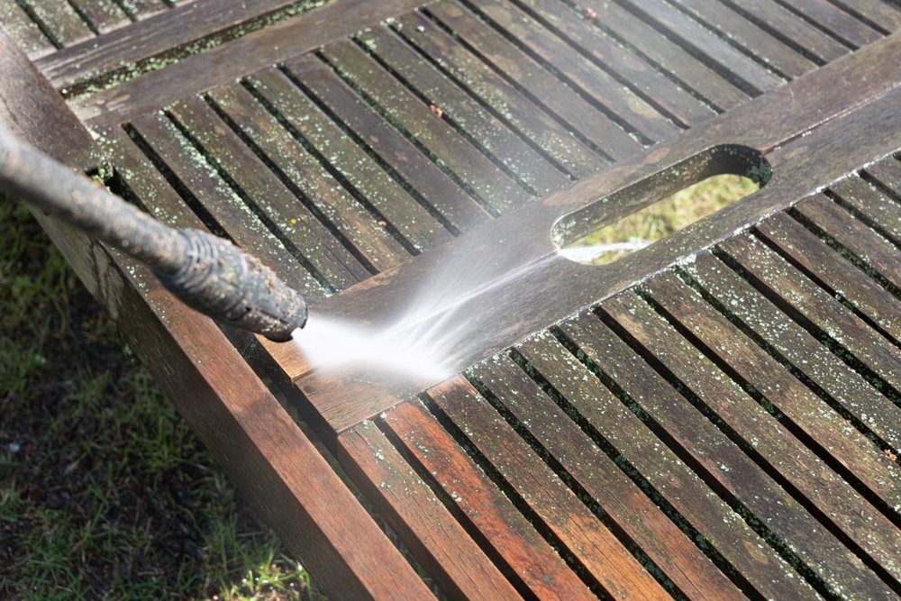A Person Is Cleaning A Wooden Table With A High Pressure Washer — The Guttering Cleaning Man in Nabiac, NSW