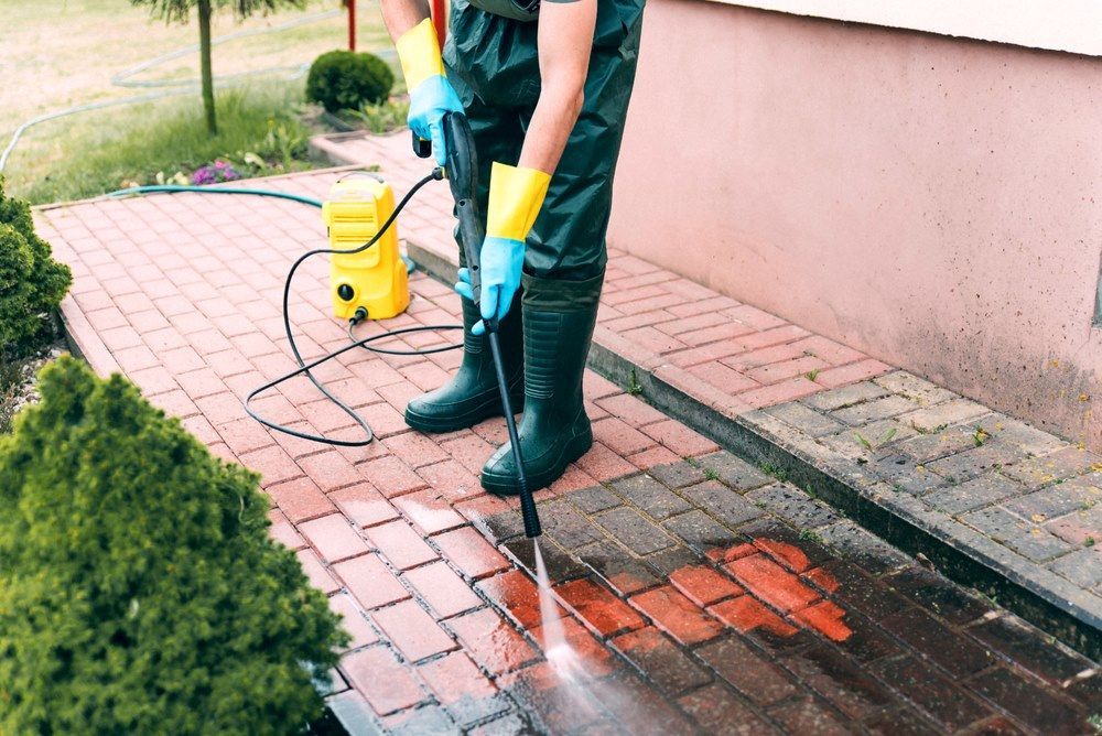 A Man Is Using A High Pressure Washer To Clean A Brick Walkway — The Guttering Cleaning Man in Nabiac, NSW