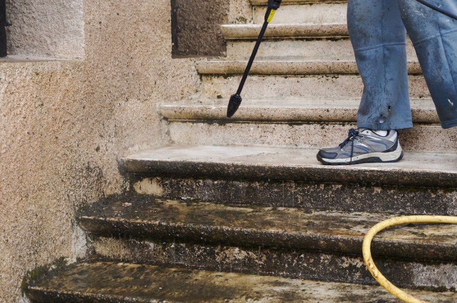 A Person Is Cleaning A Set Of Stairs With A High Pressure Washer — The Guttering Cleaning Man in Pacific Palms, NSW