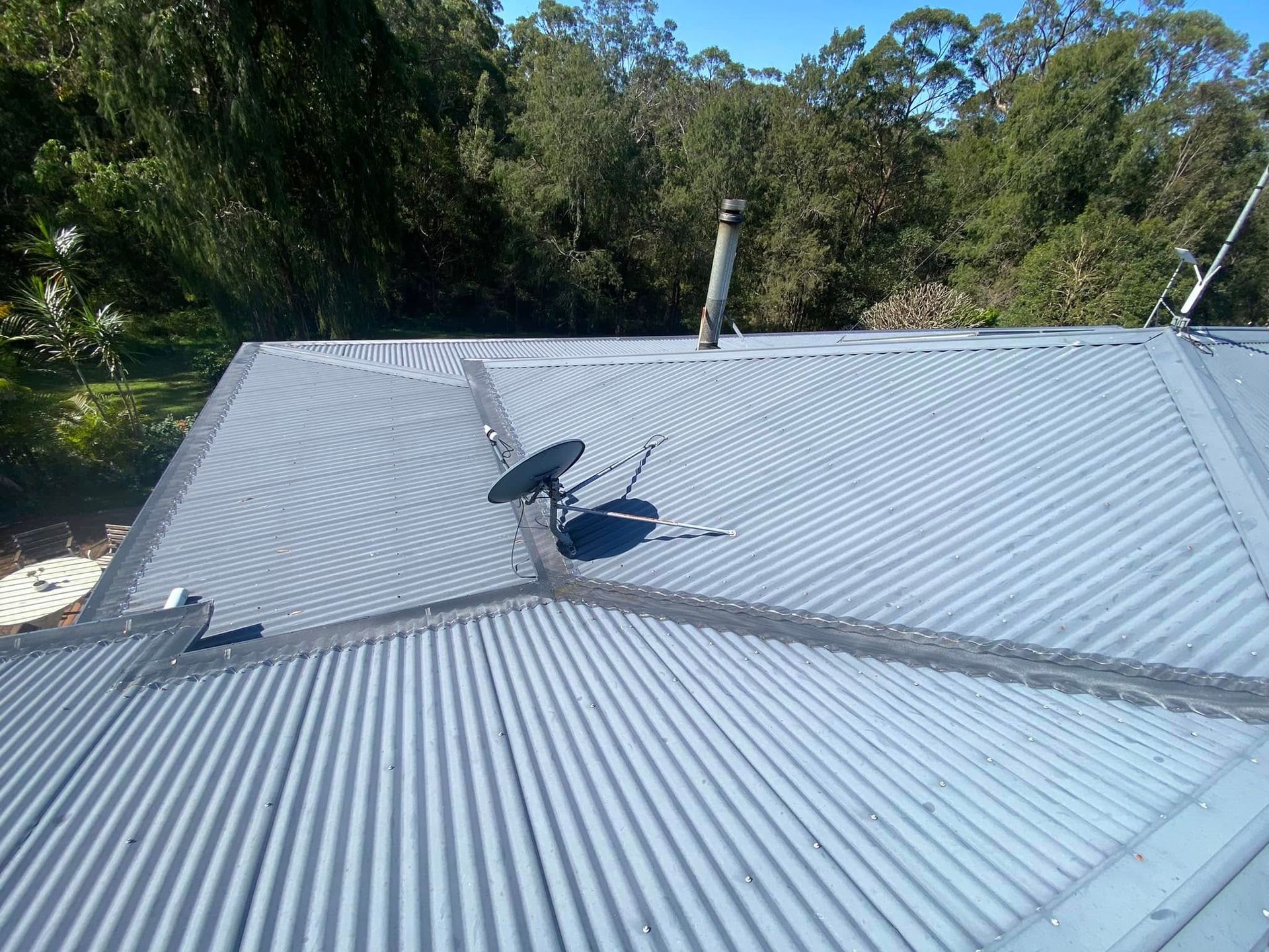 A Blue Roof Of A House With A Fence And Trees In The Background — The Guttering Cleaning Man in Forster, NSW