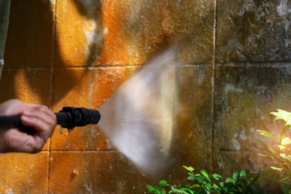 A Person Is Using A High Pressure Washer To Clean A Wall — The Guttering Cleaning Man in Taree, NSW