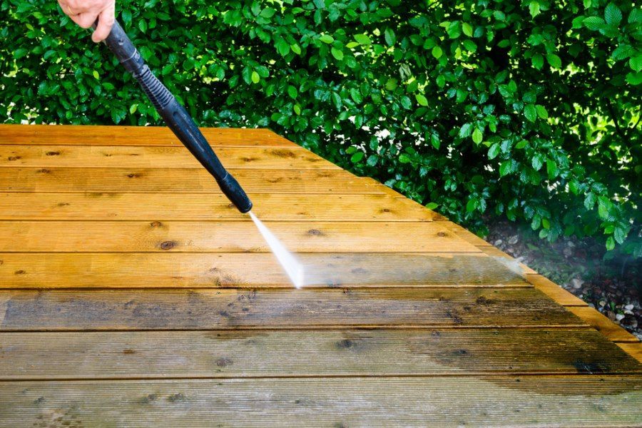 A Person Is Using A High Pressure Washer To Clean A Wooden Deck — The Guttering Cleaning Man in Wingham, NSW