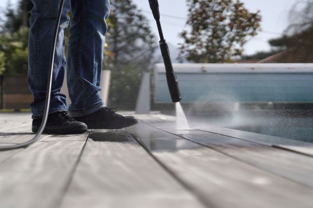 A Person Is Cleaning A Wooden Deck With A High Pressure Washer — The Guttering Cleaning Man in Old Bar, NSW
