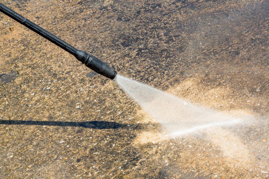 A person is using a high pressure washer to clean a concrete surface.
