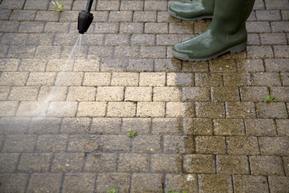 A Person Is Cleaning A Brick Walkway With A High Pressure Washer — The Guttering Cleaning Man in Tuncurry, NSW