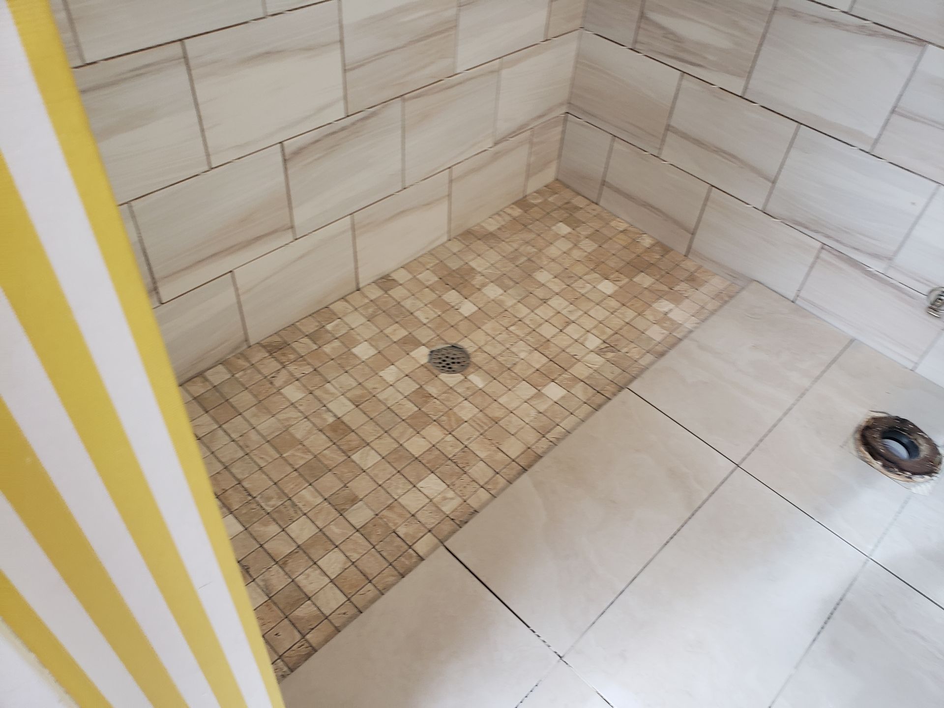 Tiled shower corner with beige wall tiles, mosaic shower floor, and two drain openings