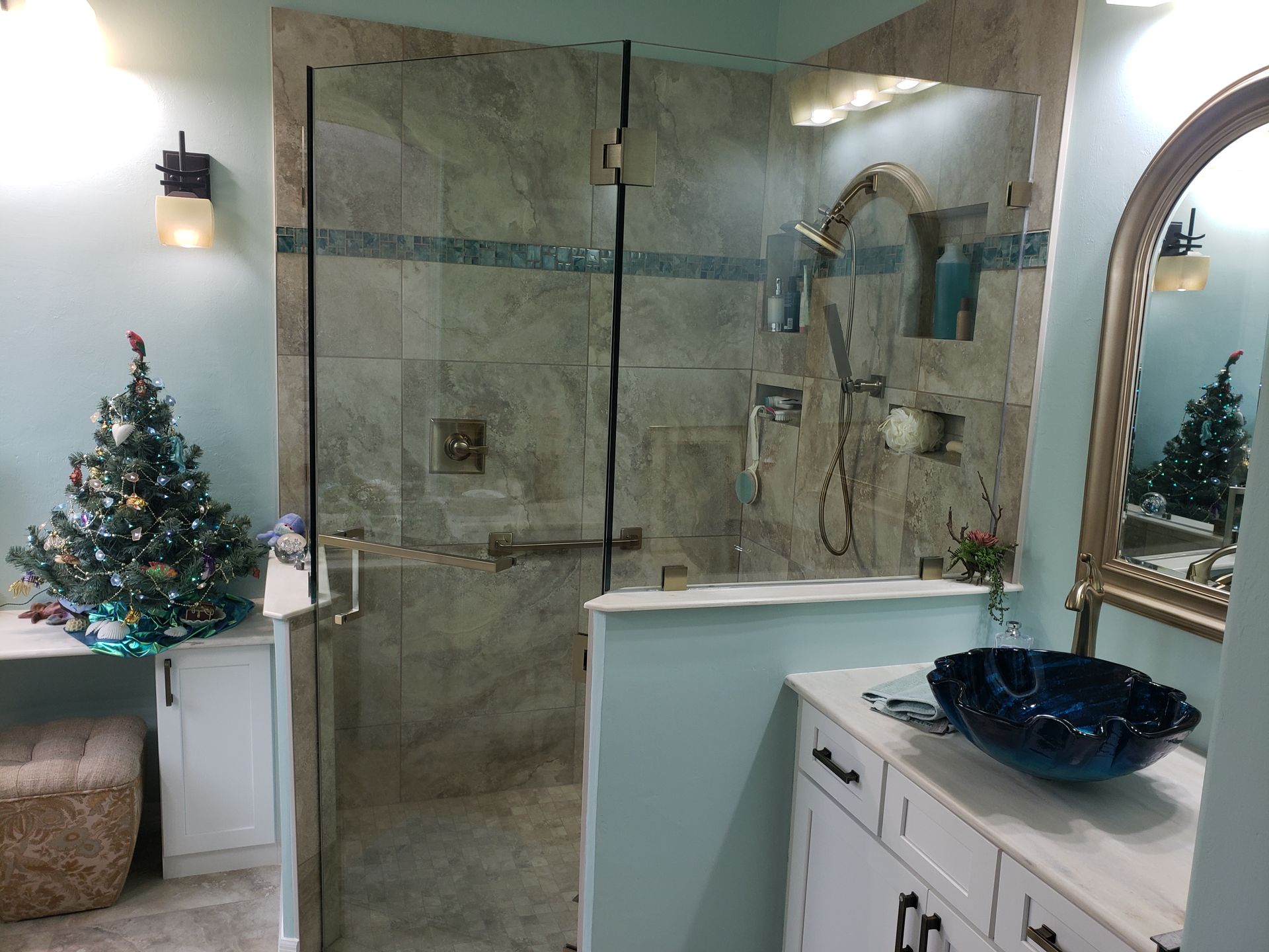 Bathroom with glass shower, white vanity, blue vessel sink, and small decorated Christmas tree.