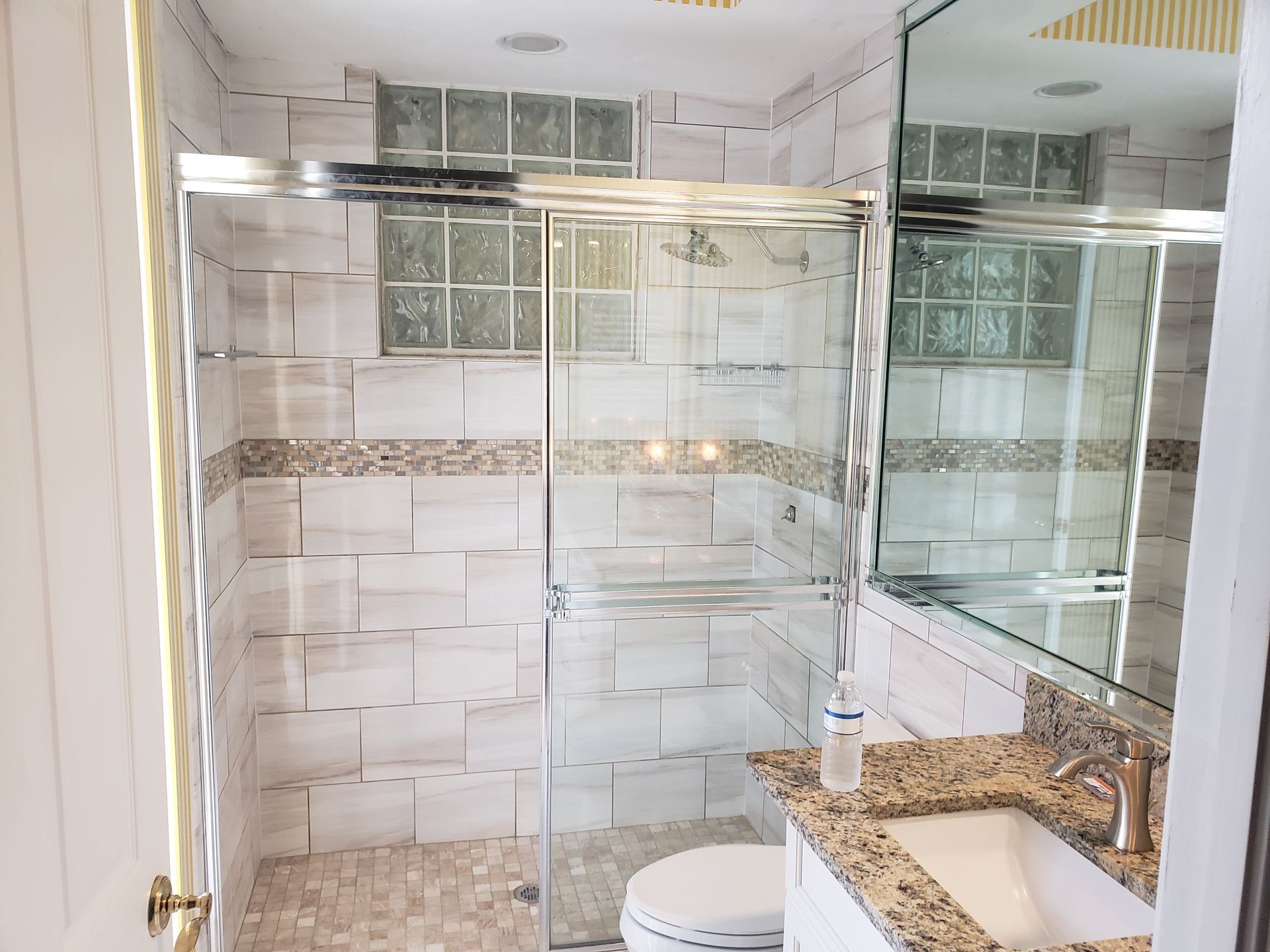 Modern bathroom with glass shower, white tile walls, and granite vanity sink