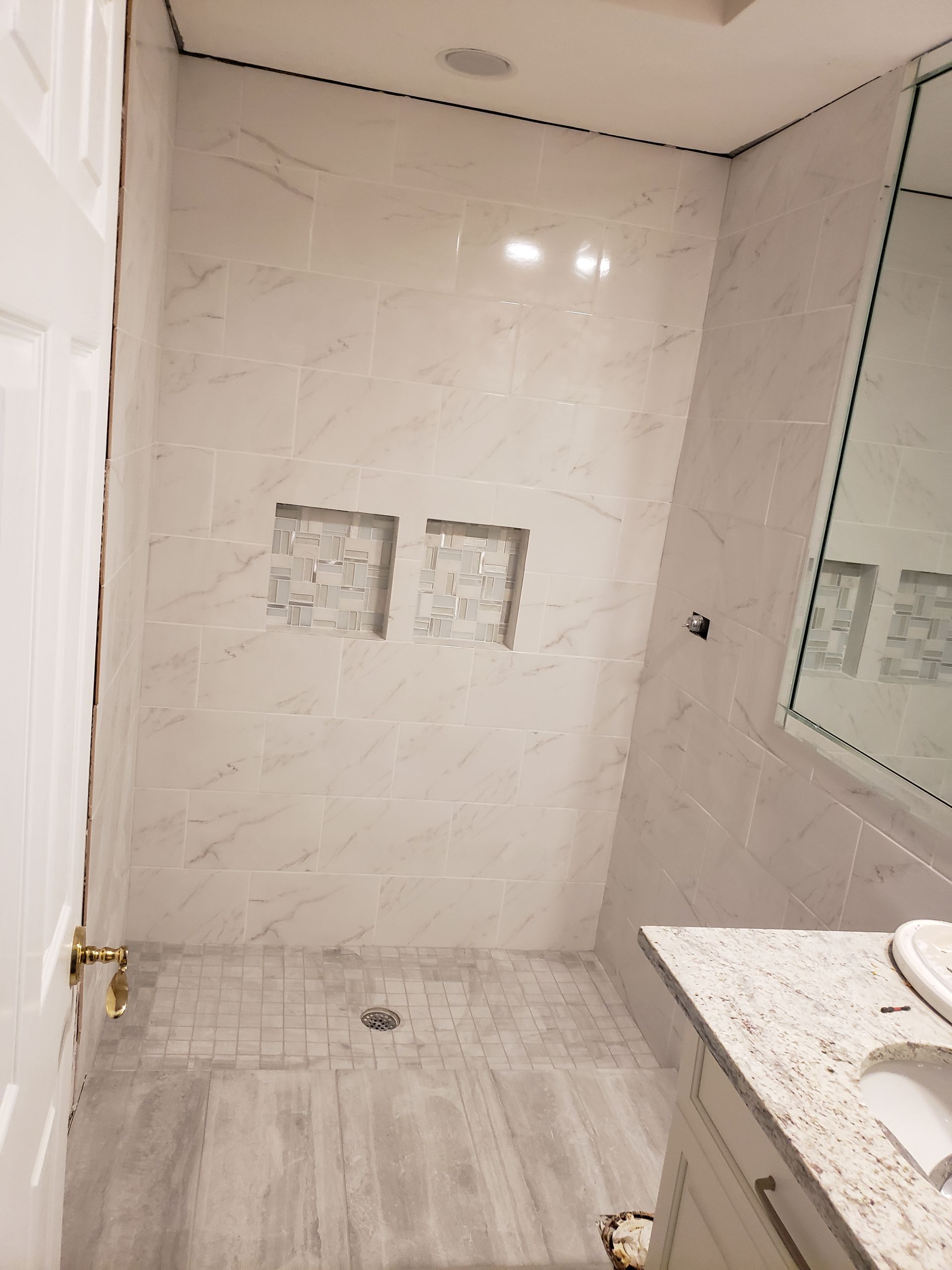 Empty tiled bathroom with a shower wall, glass panel, and vanity sink.