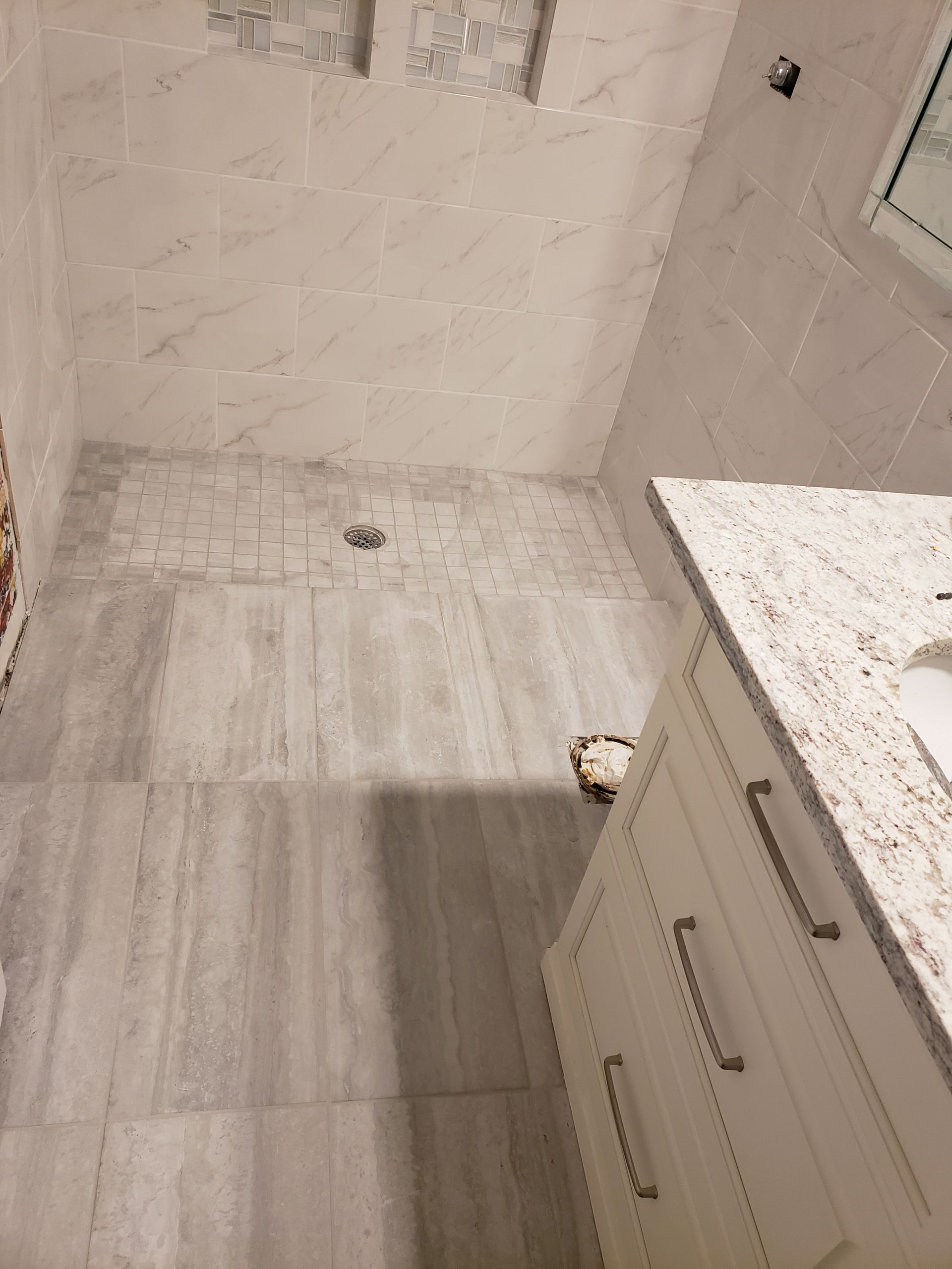 Small bathroom corner with tiled shower floor, white walls, and a vanity cabinet with sink edge.