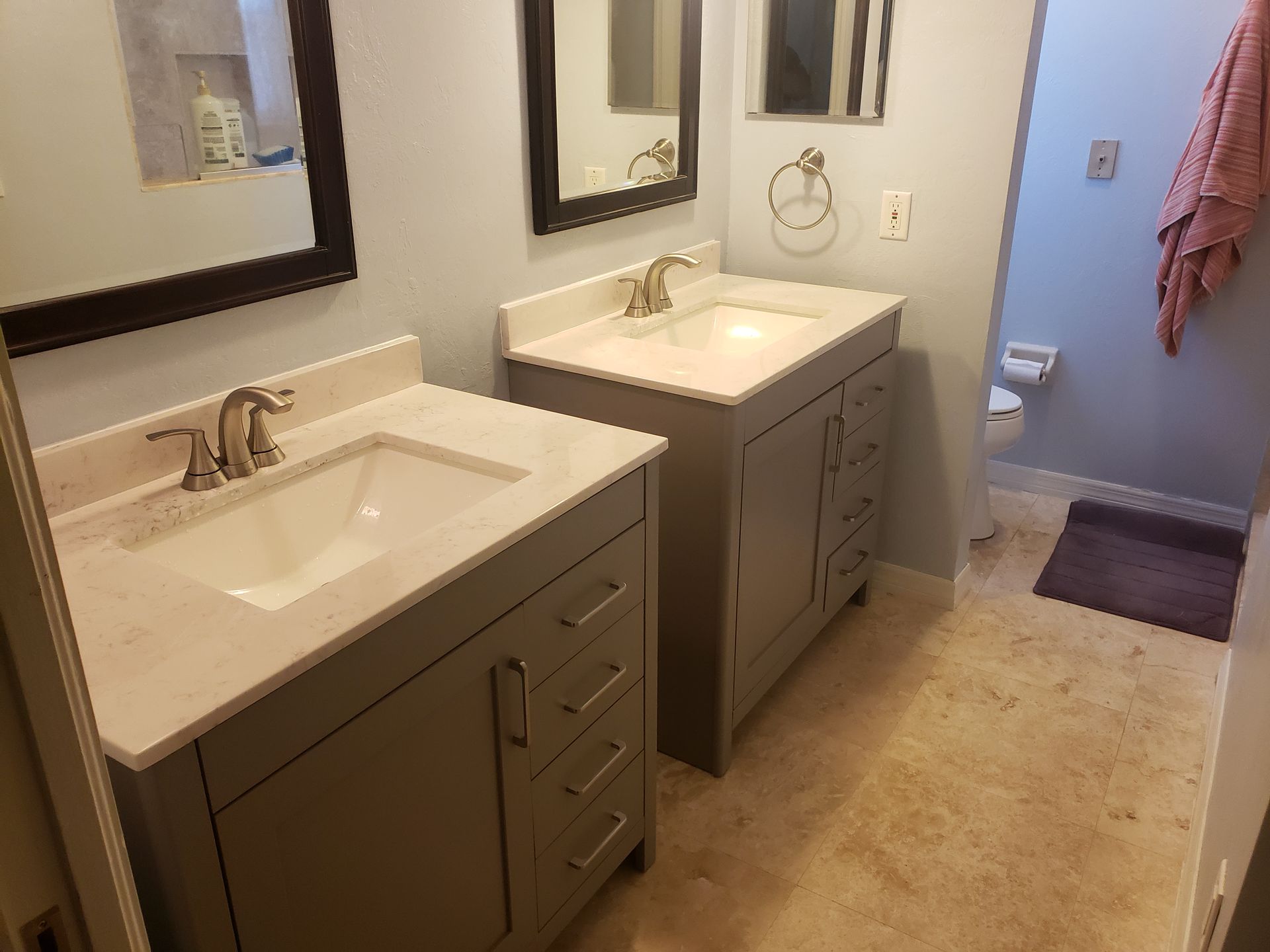 Bathroom with two white sinks, mirrors, and gray vanities on a beige tile floor.