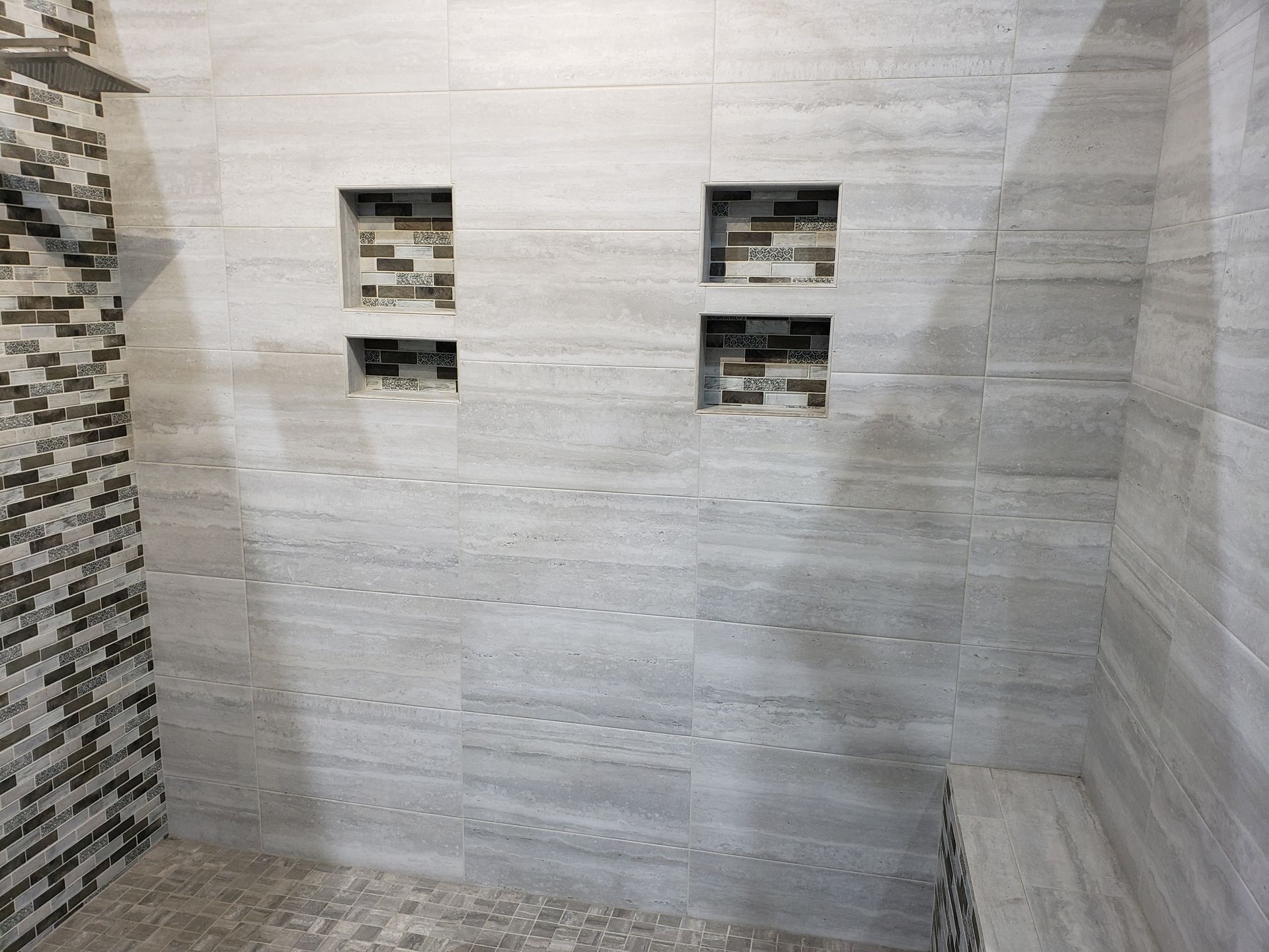 Modern tiled shower wall with four square niches and a mosaic accent strip on the left