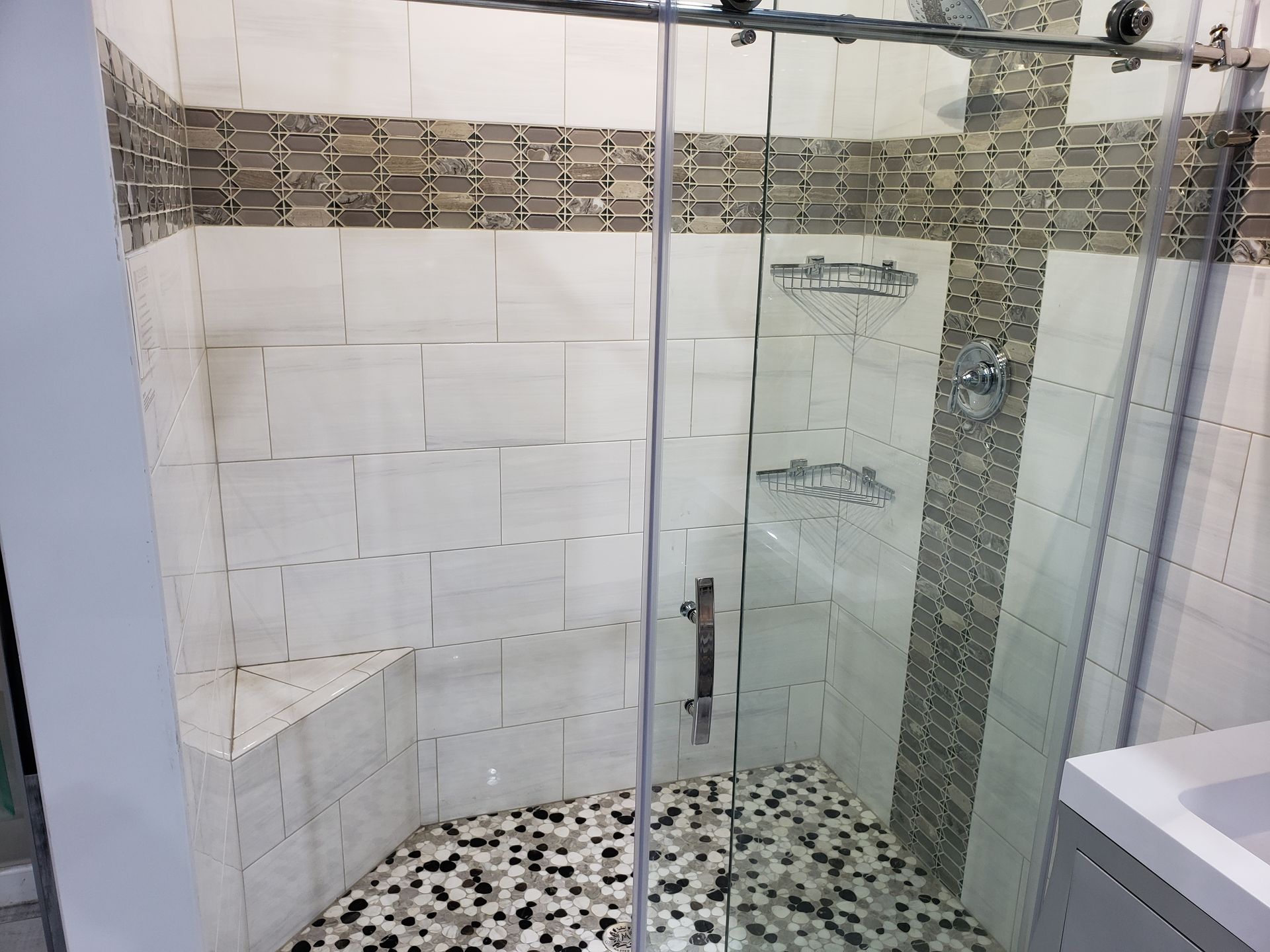 Glass shower with mosaic floor and white tile walls in a bathroom