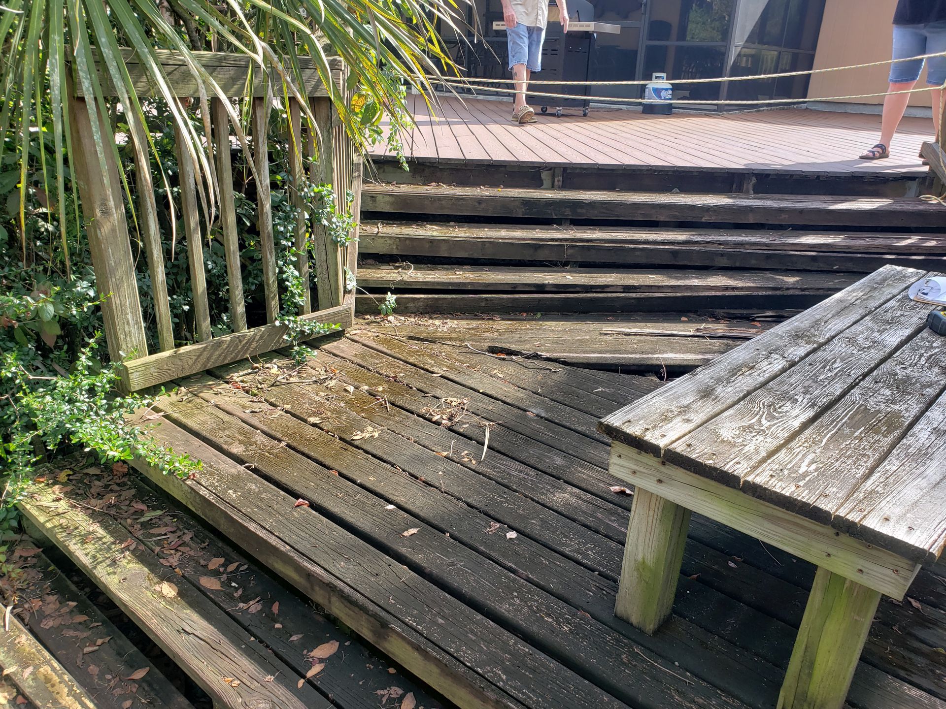 Weathered wooden deck with steps, railing, and a bench in a sunny outdoor setting